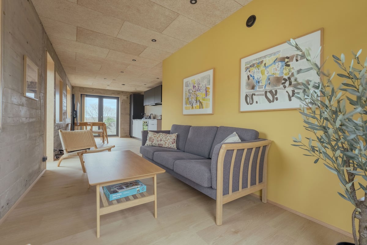 Ein Wohnzimmer mit einer Couch, einem Couchtisch und einer Pflanze. An den Wänden hängen gerahmte Bilder.