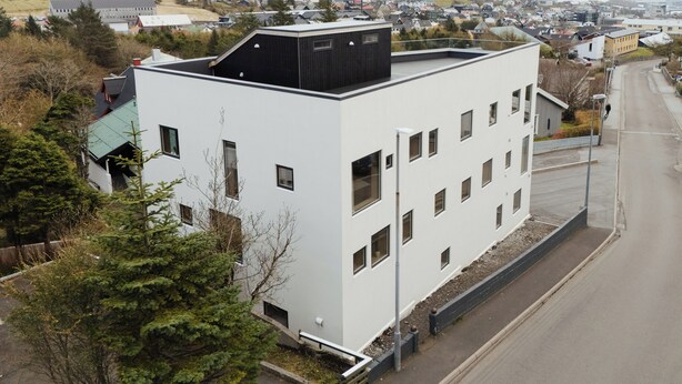 A modern building with a flat roof, multiple windows, and a view of a coastal town. - A Varoa Apartments (Torshavn)