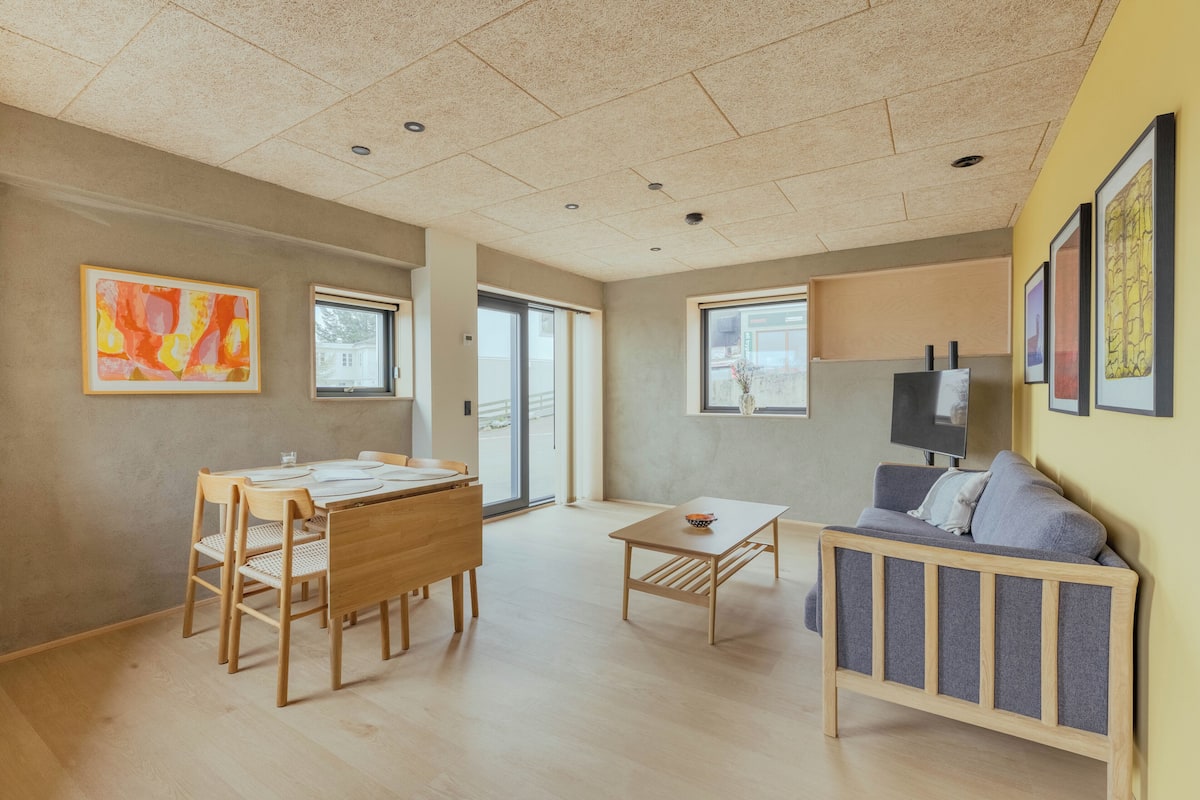 Ein modernes Wohnzimmer mit Esstisch, Sofa und Kunstwerken an den Wänden.