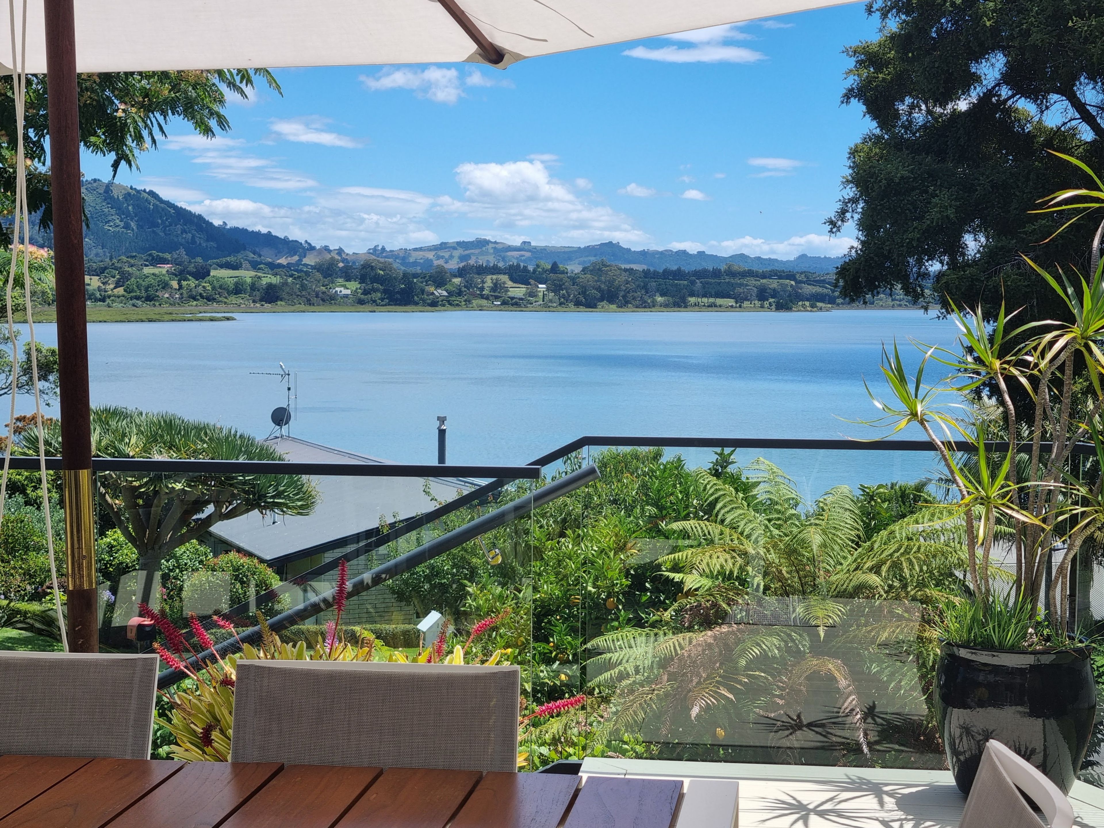 A terrace with a view of a lake, surrounded by lush greenery and a clear sky.