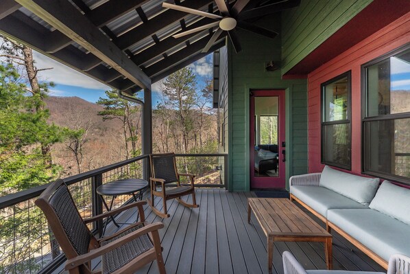 A covered porch with a wooden table, two rocking chairs, and a sofa.