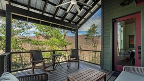 Un espacio al aire libre techado con mobiliario de madera, incluyendo sillas y una mesa, y vistas del paisaje circundante.
