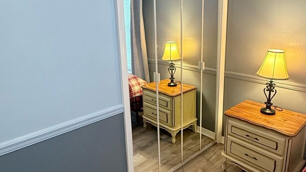 Une chambre avec un grand miroir, deux tables de chevet avec des lampes, un plancher en bois et une couvre-lit à carreaux.
