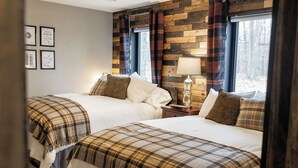Une chambre avec deux lits, chacun recouvert d’une couette à carreaux, une table de chevet avec une lampe et une fenêtre avec des rideaux.