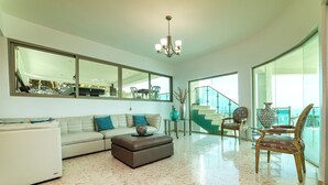 A spacious living room with a large mirror, a chandelier, a sofa, an ottoman, and a chair.