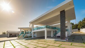 A modern multi-level house with a glass balcony, a staircase, and a paved outdoor area.