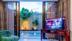 A modern hotel room with a large TV, a green sofa, a yellow bedspread, and a view of a brick wall and plants outside. - Fuwan Haitao Meishu Lingshui Haitang Bay (Lingshui)