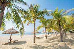 A beach with palm trees, thatched umbrellas, and wooden lounge chairs. - Fuwan Haitao Meishu Lingshui Haitang Bay (Lingshui)