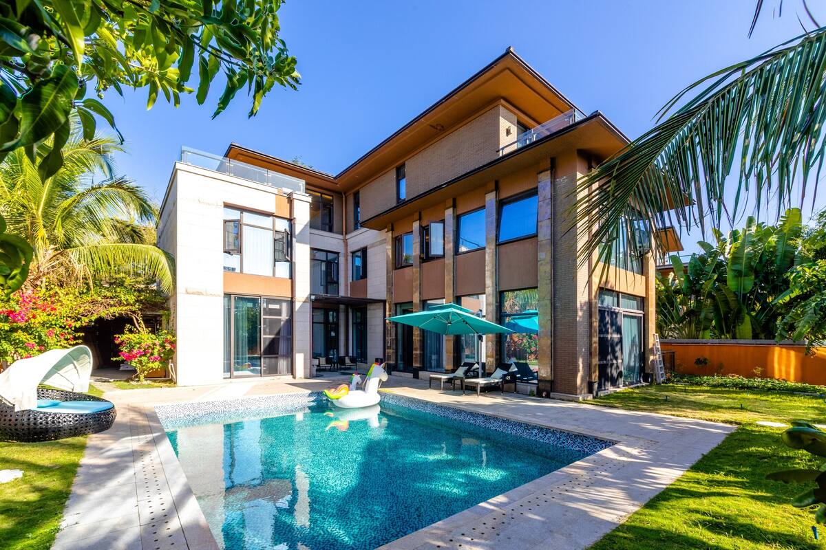 A modern house with a swimming pool, surrounded by lush greenery and palm trees.