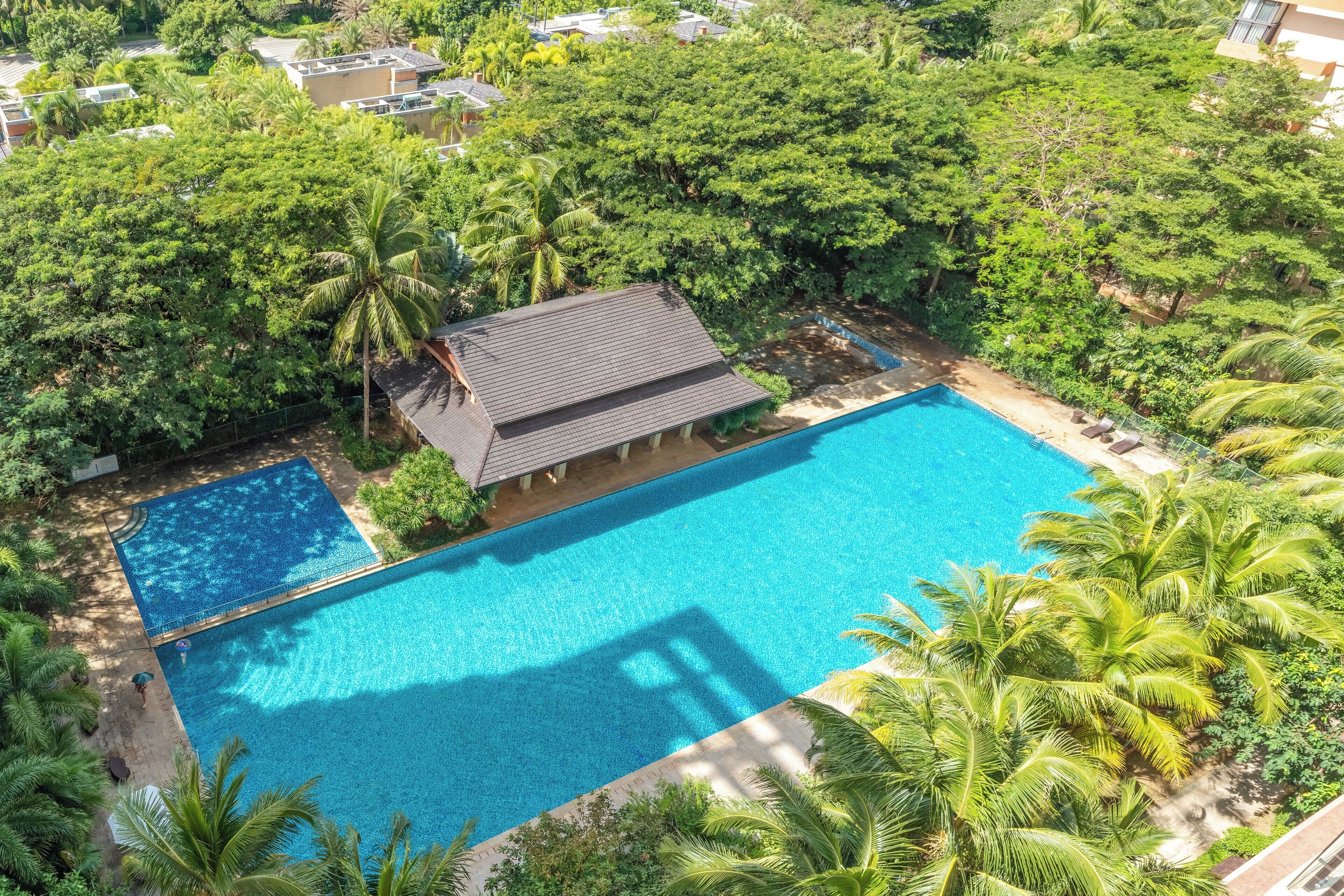 An aerial view of a resort with a large swimming pool surrounded by lush greenery and palm trees.