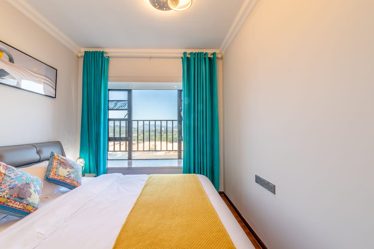 A hotel room with a bed, a view of the balcony, and a painting on the wall.