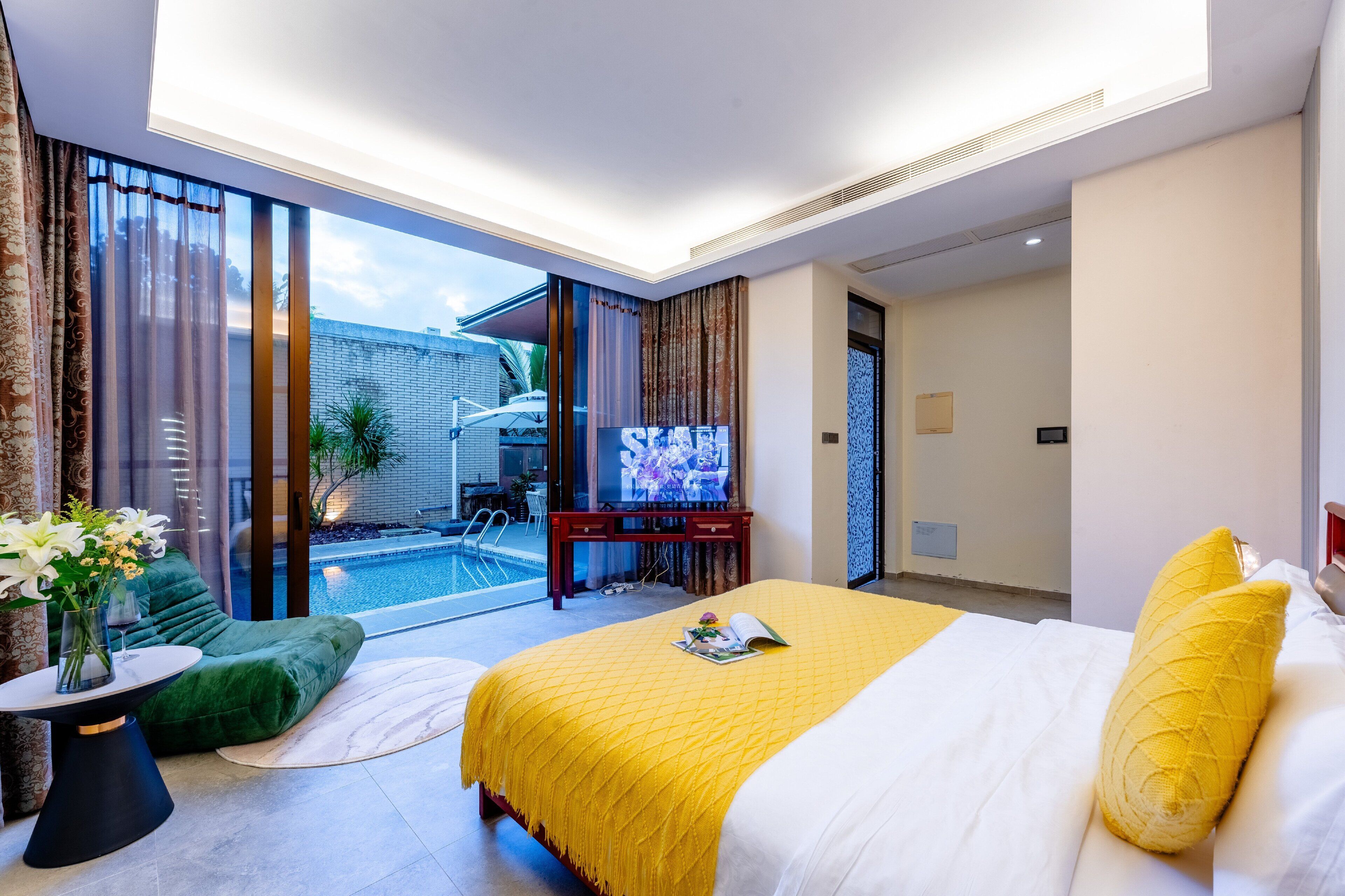 Ein Hotelzimmer mit einem großen Bett, einem Fernseher, einem kleinen Pool und einem Balkon mit Vorhängen.