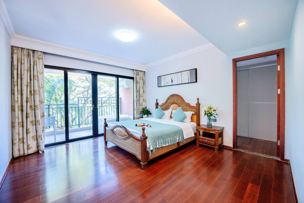 A spacious bedroom with a large bed, wooden floor, and a balcony with curtains.