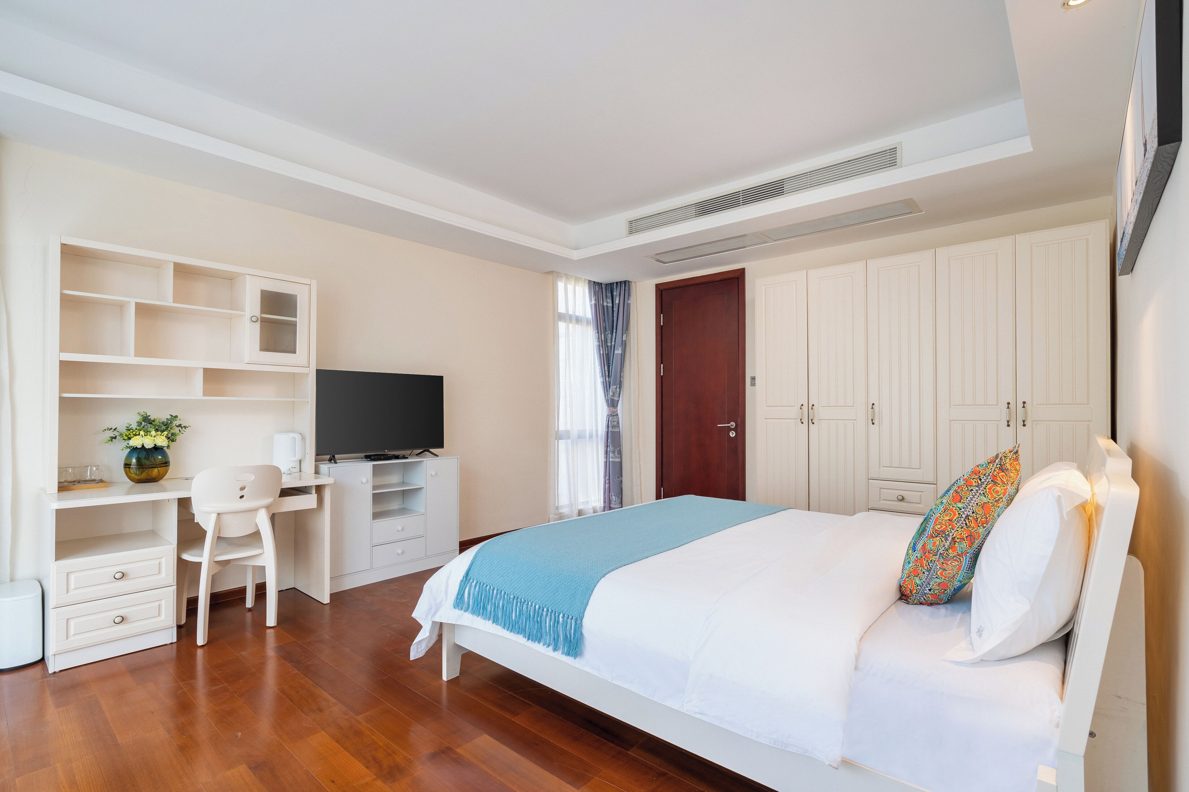 A bedroom with a bed, a desk, a chair, a television, and a wardrobe.