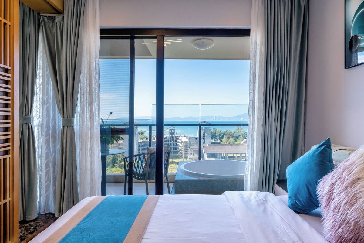 A hotel room with a large bed, a view of the city, and a balcony with a hot tub.