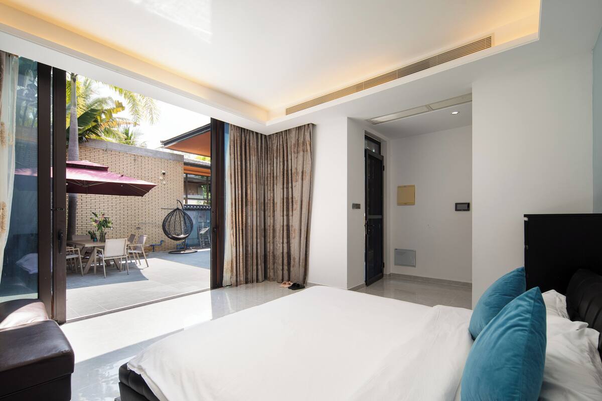 A modern hotel room with a large bed, a desk, and a view of the outdoor area.