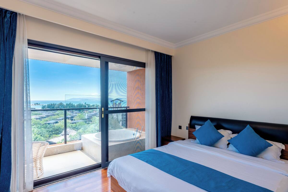 A hotel room with a large bed, a view of a cityscape, and a balcony with a hot tub.