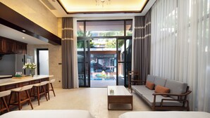 A modern hotel room with a kitchen area, a seating area with a sofa and chairs, and a large sliding glass door leading to a pool. - Fuwan Haitao Meishu Lingshui Haitang Bay (Lingshui)