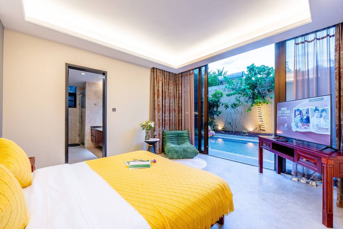 A modern hotel room with a large bed, a TV, and a view of a swimming pool.