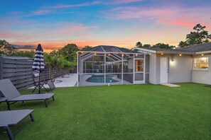 Un patio trasero con piscina, un porche techado y mobiliario de exterior.