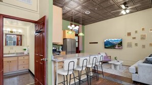 Una cocina compacta con barra, una zona de comedor con taburetes altos, un sofá y un televisor.