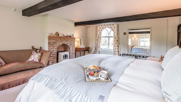 A cozy bedroom with a large bed, a fireplace, a sofa, and a window with curtains. - Mulberry End, Foxhall (Foxhall)