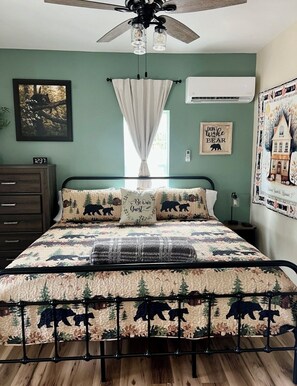 A bedroom with a bed featuring a bear-themed quilt, a ceiling fan, an air conditioning unit, a nightstand, and a wall clock. - Baybeary Cottage, Bayfield base camp for Fun, Family & Adventure near Durango (Bayfield)
