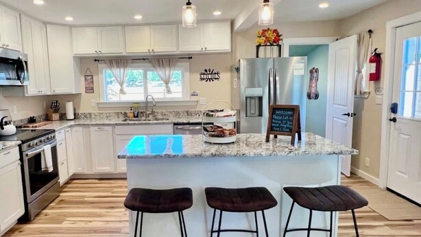 A modern kitchen with white cabinets, a granite countertop, and a central island with stools. - Baybeary Cottage, Bayfield base camp for Fun, Family & Adventure near Durango (Bayfield)