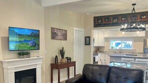 A living room with a fireplace, a leather sofa, a coffee table, a TV, and a kitchen in the background. - Baybeary Cottage, Bayfield base camp for Fun, Family & Adventure near Durango (Bayfield)