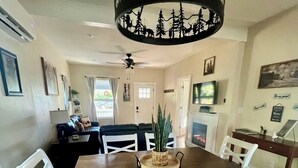 A dining area with a wooden table, white chairs, a chandelier, and a blue patterned rug. - Baybeary Cottage, Bayfield base camp for Fun, Family & Adventure near Durango (Bayfield)