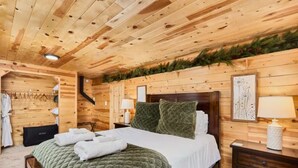 A wooden cabin-style bedroom with a bed, nightstands, a dresser, and a closet with hanging clothes. - Family Cabin • Hot Tub • Disc Golf • Forest Access (Divide)
