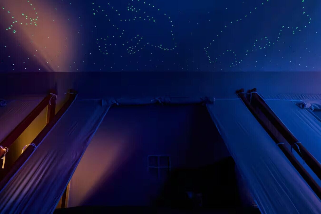 Un dormitorio con literas, una ventana y una proyección del cielo estrellado en el techo.