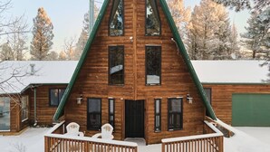 A wooden cabin with a steeply pitched roof, a balcony with railings, and a snow-covered ground. - Family Cabin • Hot Tub • Disc Golf • Forest Access (Divide)