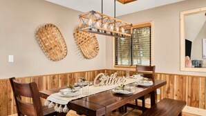 A dining area with a wooden table set for four, a bench, and a hanging light fixture. - Family Cabin • Hot Tub • Disc Golf • Forest Access (Divide)
