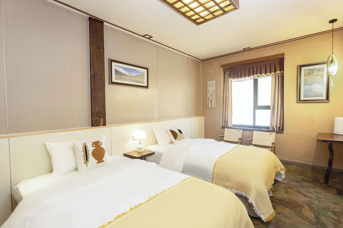 Een hotelkamer met twee bedden, een nachtkastje, een raam met gordijnen, een bureau en een wandlamp.