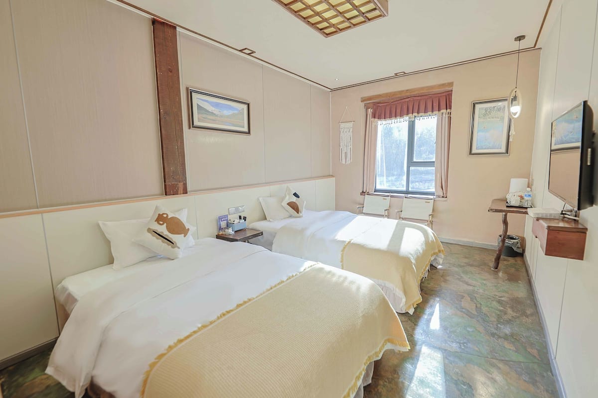 Een hotelkamer met twee bedden, een raam met gordijnen, een bureau met stoel en een televisie aan de muur.