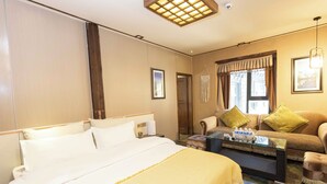A hotel room with a large bed, a sofa, a coffee table, and a view of the city through the window. - Daocheng Yading Shiruo Hotel (Garze)