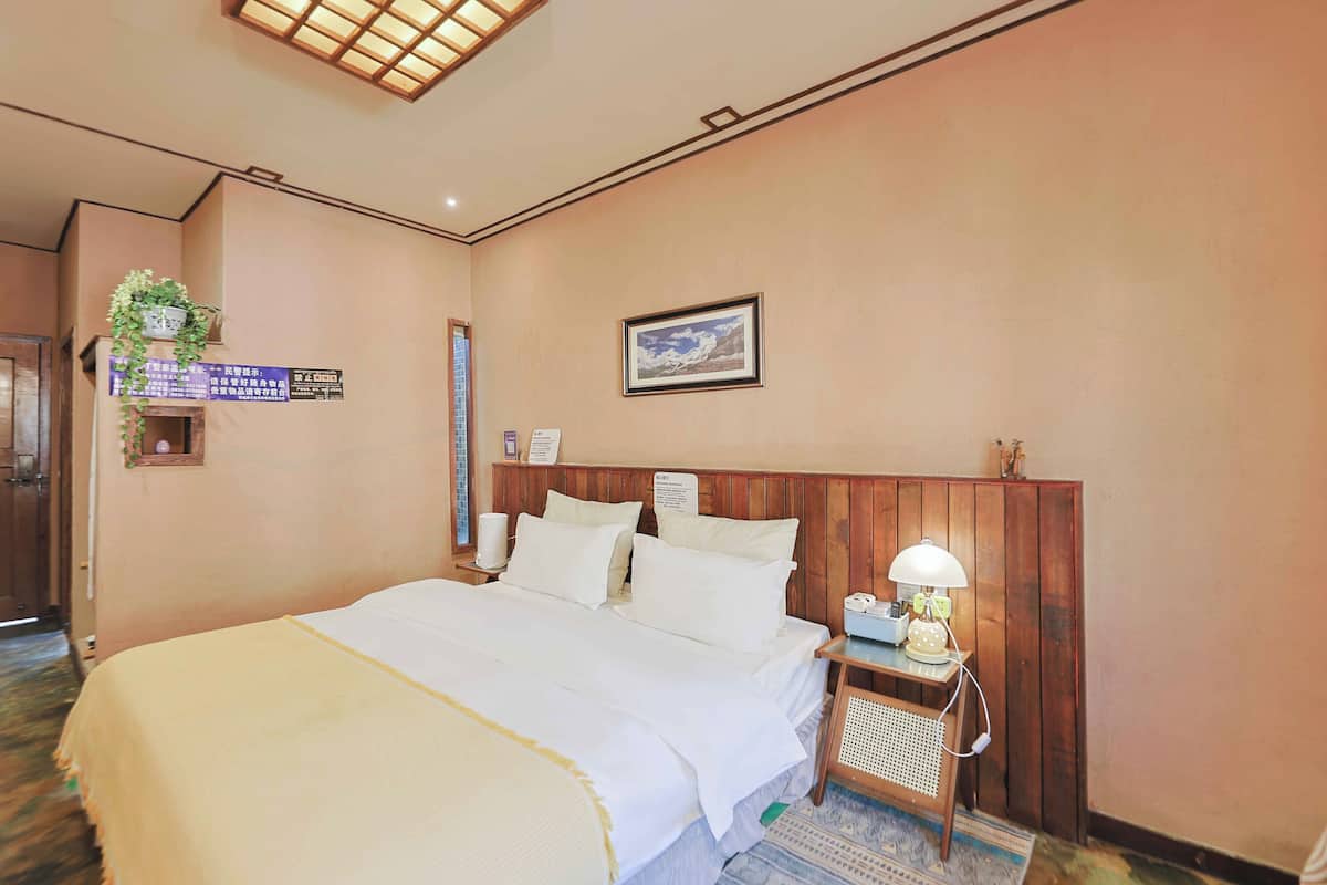Een hotelkamer met een groot bed, een houten hoofdeinde, een nachtkastje met een lamp en een lijst met een afbeelding aan de muur.
