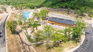 Vista aérea de un resort con piscina, un edificio grande de techo plano y un estacionamiento.