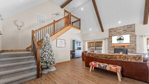 Un amplio salón con una escalera de madera, una chimenea y un árbol de Navidad.