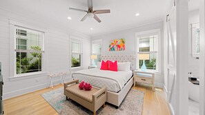 Une chambre à coucher avec un lit, un ventilateur de plafond, une table de chevet, une lampe, une fenêtre et un tableau.
