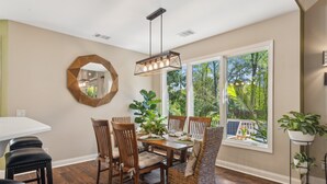 Un comedor con una mesa rectangular, seis sillas, una lámpara colgante y un amplio ventanal con vistas a la vegetación.