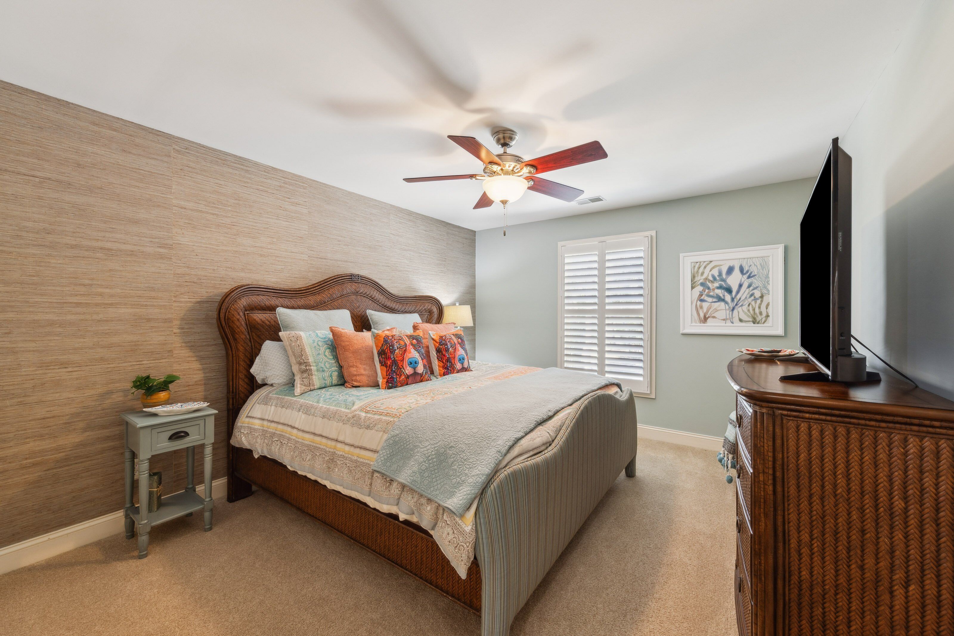 A bedroom with a wooden bed, a ceiling fan, a television, and a small side table with a plant.