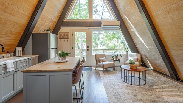 A modern kitchen with a central island, wooden flooring, and a view of the outdoors through large windows. - Jackson A Frame (Rossville)