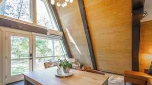 A modern interior with a wooden dining table, a sofa, and a large window providing a view of the outdoors. - Jackson A Frame (Rossville)