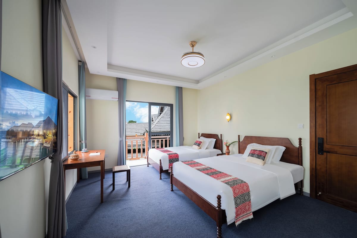 A hotel room with two beds, a desk, and a window with a view of a building.