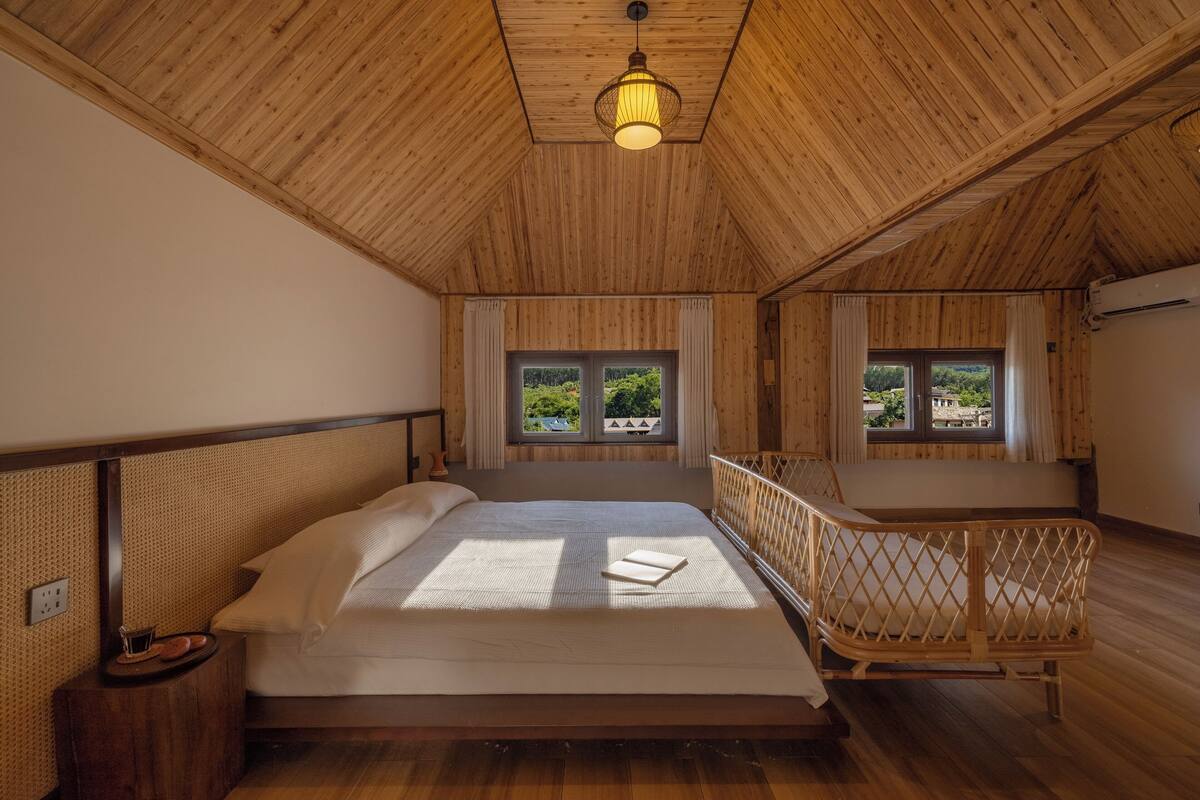 A bedroom with a wooden ceiling, a bed with white linens, a bedside table, and a window with curtains.