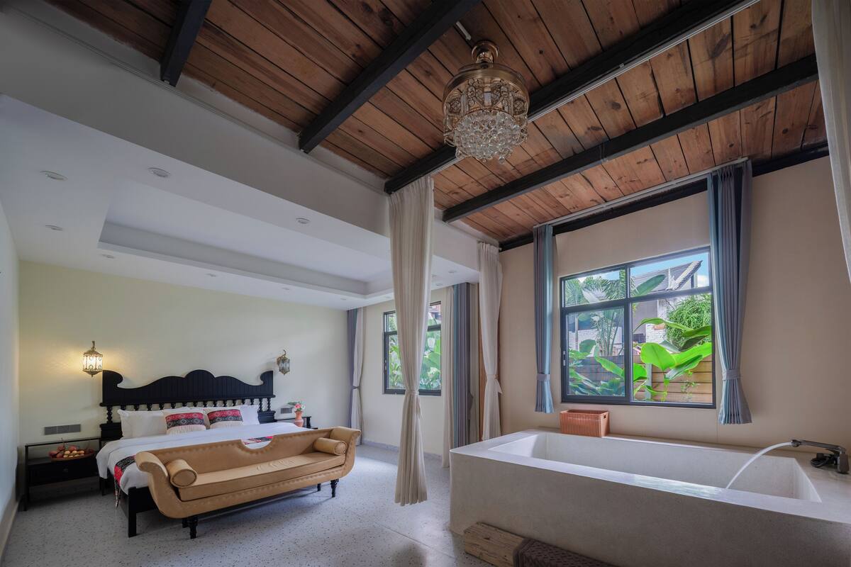 A bedroom with a bed, a sofa, a large window, and a bathtub.