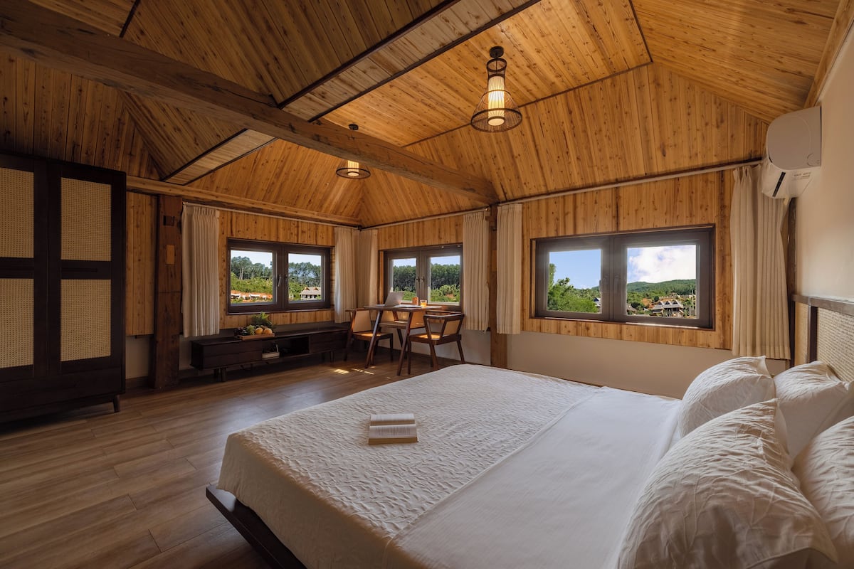 A wooden-paneled room with a bed, a desk, and a view of the outdoors.