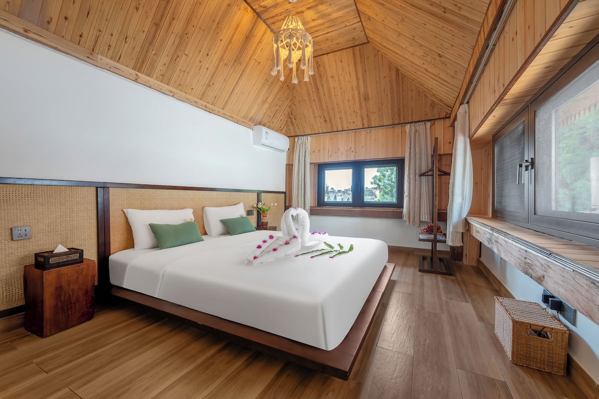 A wooden-paneled bedroom with a large bed, a window, and a wooden ceiling.